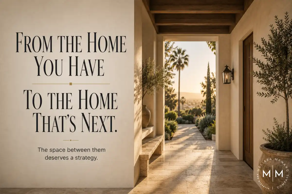 Text overlay "From The Home You Have To The Home That's Next" positioned on the left. The right side displays a covered exterior patio area. The patio features a dark stained exposed wood beam ceiling, smooth white stucco walls, and rectangular travertine stone flooring. A black metal wall sconce is mounted next to a solid wood door. The patio opens to a view of landscaping, palm trees, and distant hills under a clear sky.