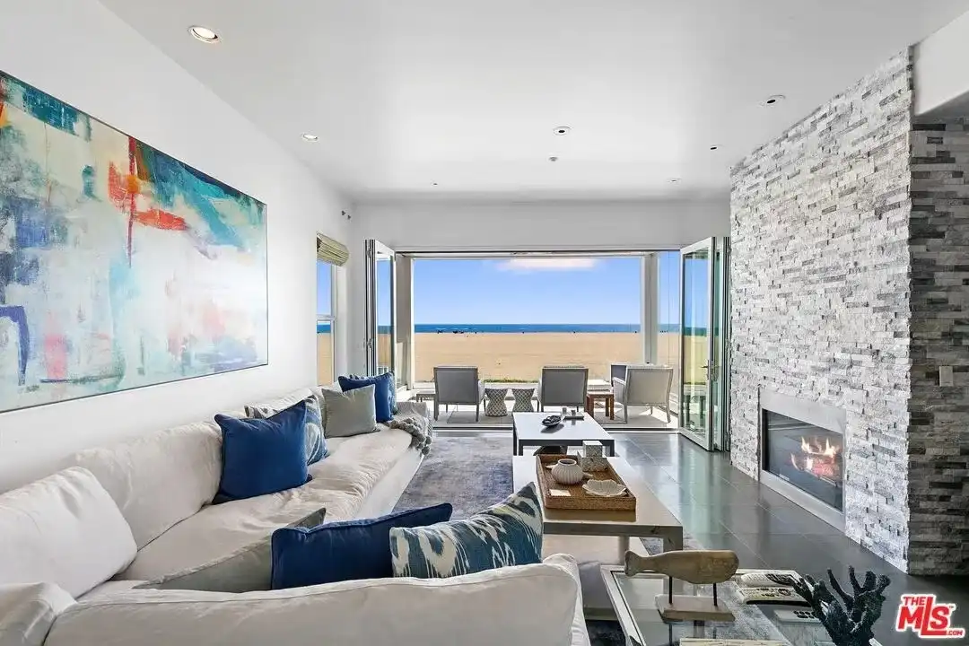 Modern living room with white sectional, blue pillows, and floor-to-ceiling stacked stone fireplace.