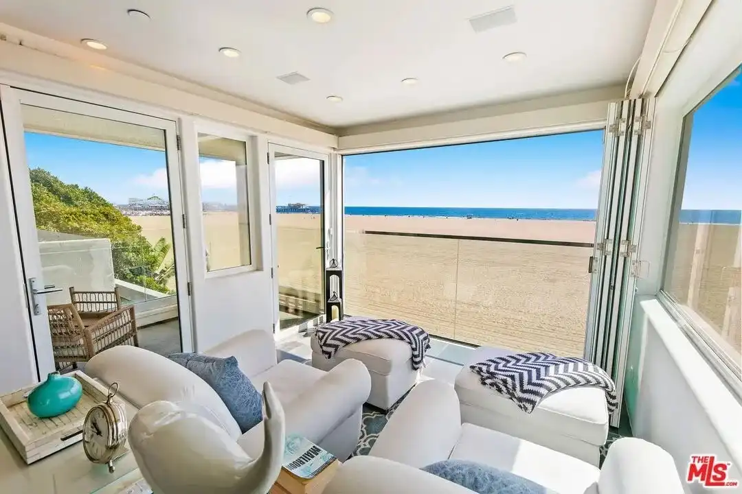 Sunroom with white armchairs, chevron patterned throws, and folding glass doors opening to beach.