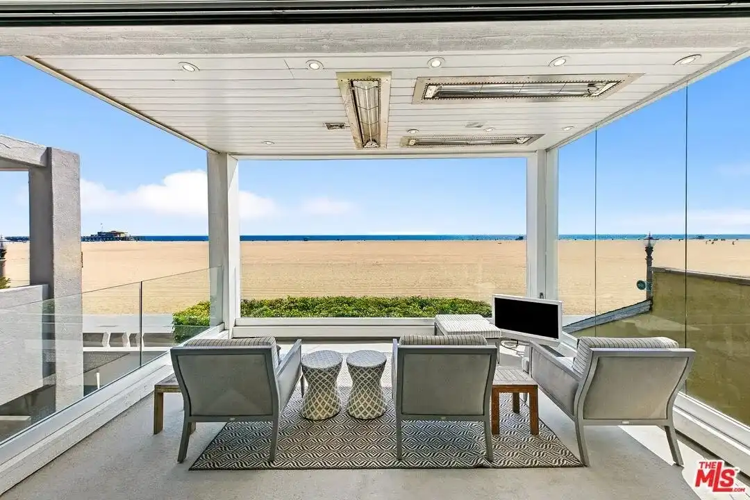 Covered patio with recessed lighting, outdoor heaters, gray armchairs, and direct beach view.