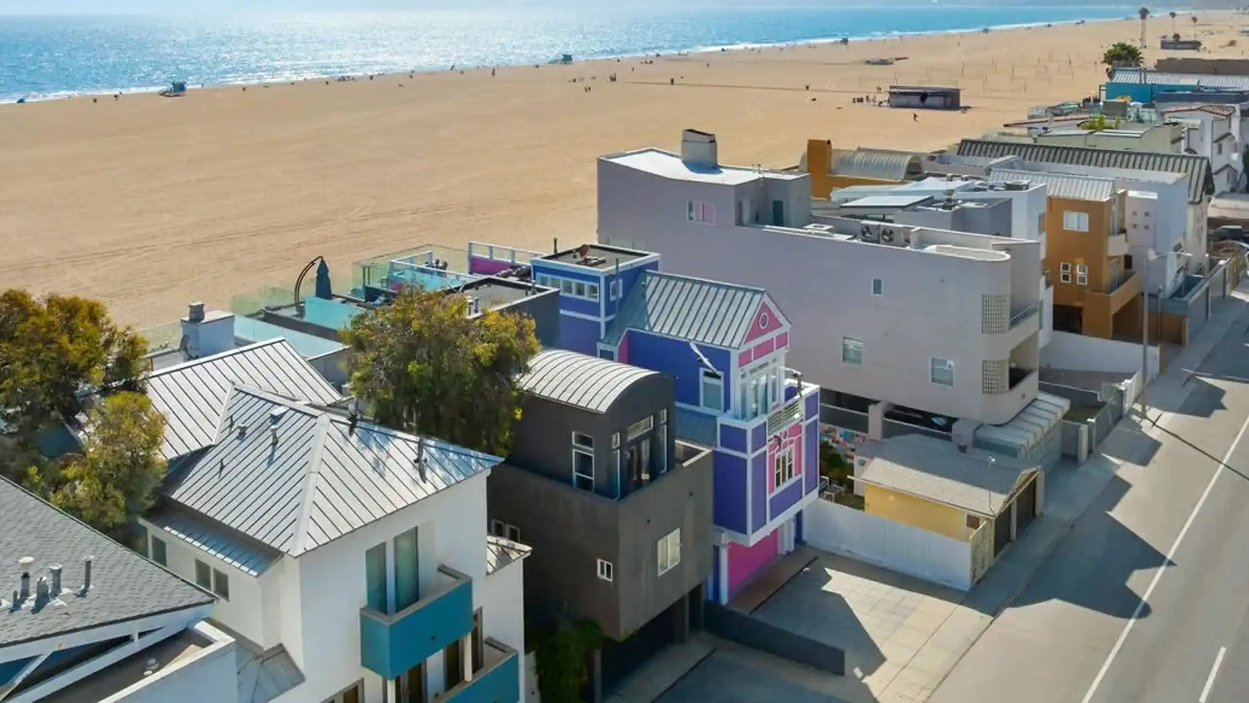 Aerial view of multi-story beachfront residential buildings along a sandy shoreline and paved road.