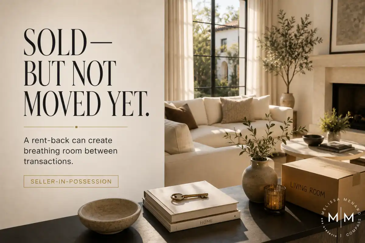 Text graphic stating "Sold - But Not Moved Yet" on the left. The right side shows a bright living room interior. A dark wood console table in the foreground holds a cardboard box labeled "Living Room," a book with a brass key, and a small vase with greenery. In the background, a white fabric sectional sofa sits in front of multi-pane black metal windows. A stone fireplace mantel is visible on the far right.