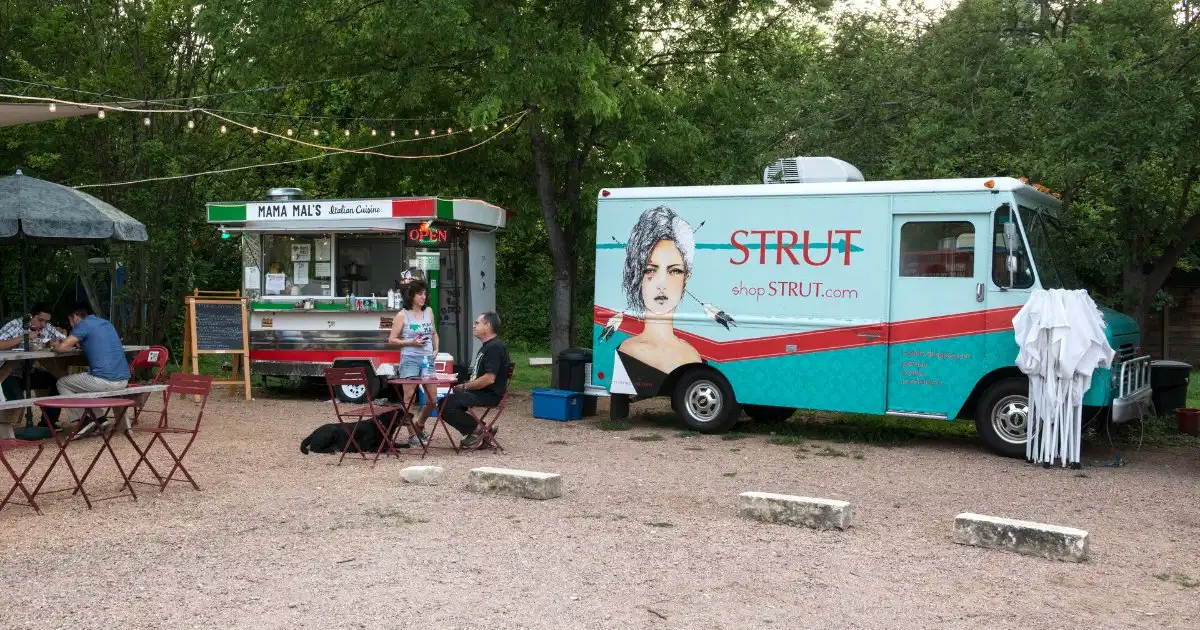 Colorful food trucks parked under shade trees in South Austin