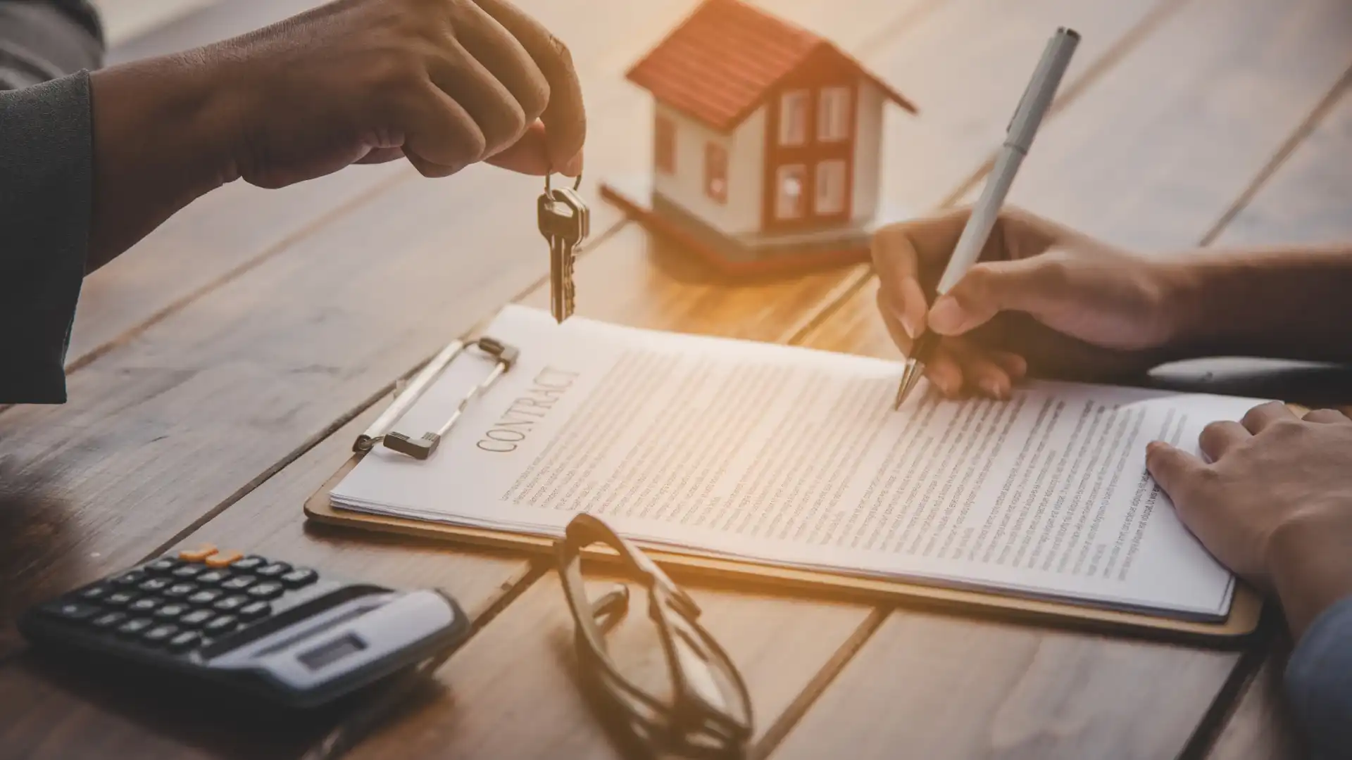 Hands signing a real estate contract with house keys being handed over and a miniature house model on a wooden table representing the Nashville home closing process