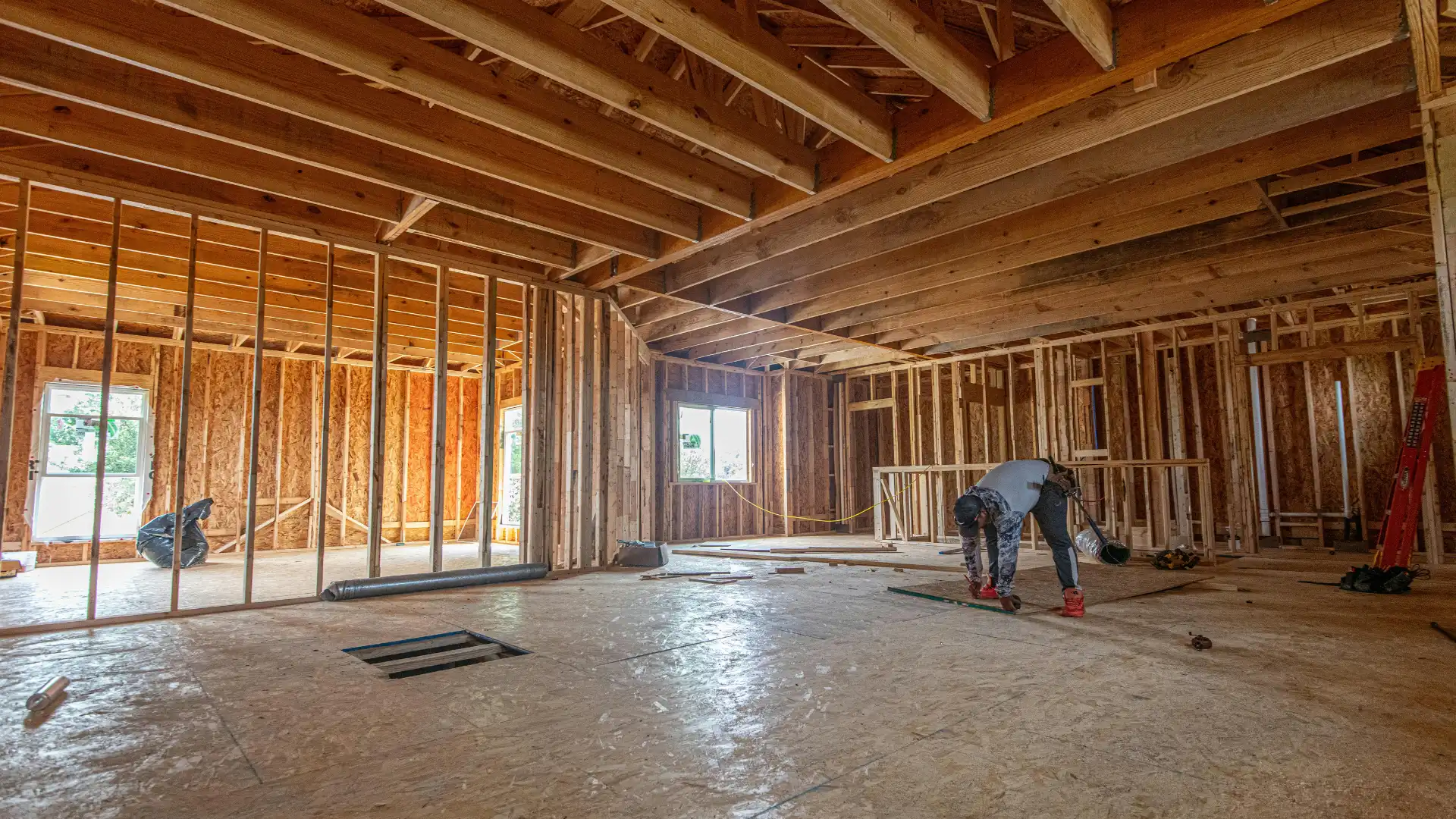 Interior framing of a Nashville custom home under construction, with exposed wood wall studs, open subfloor, cathedral ceiling joists, and a builder working in the foreground