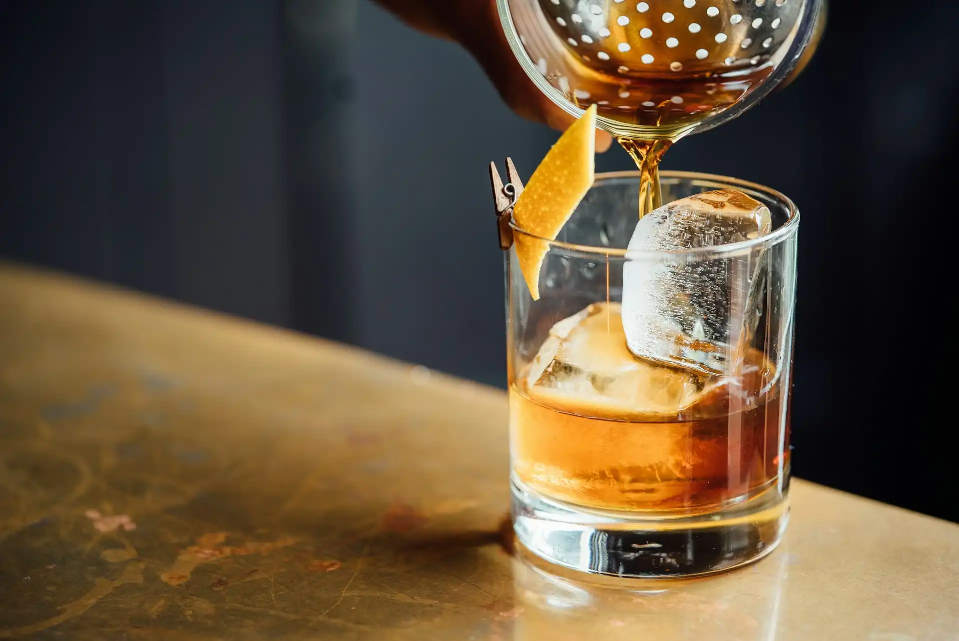 A bartender pouring an amber cocktail over a large ice cube