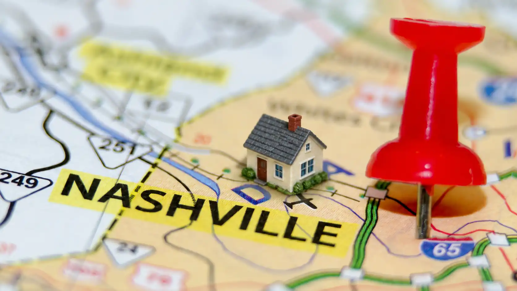 Close-up photograph of a Nashville Tennessee road map with a miniature house and red pushpin marking Nashville representing luxury home search